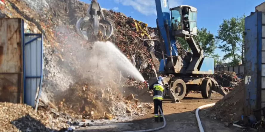 There is a fire in the waste sorting plant. In the picture, you can see a firefighter extinguishing the waste, and an excavator is being used to chew through the waste and catch up with it.